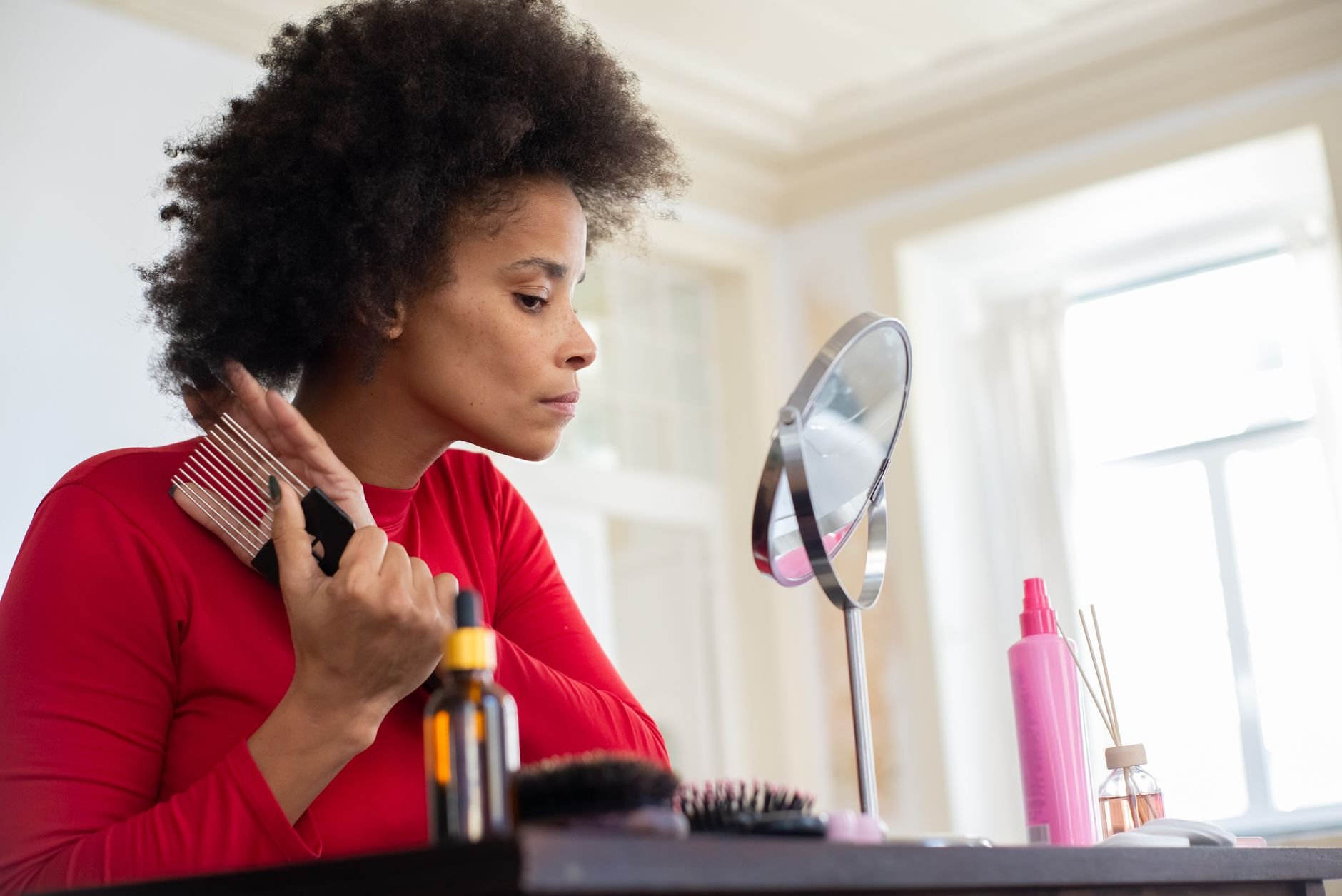 A woman combing her hair at a vanity mirror — the ritual of styling